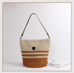 Close-up of a striped woven bucket bag with brown leather strap and shield detail