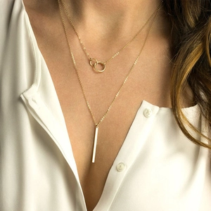 Double layer gold necklace with interlocking rings and bar pendant on a female model
