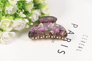Detail of floral acrylic hair claw clip with purple and gold fragments on white background