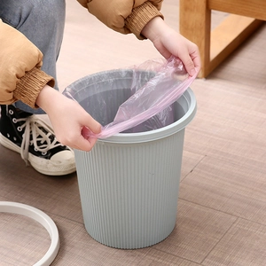 Person placing a pink disposable plastic trash bag into a grey striped household waste bin