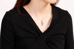 Detail of silver fish pendant necklace worn by model against a black V-neck top