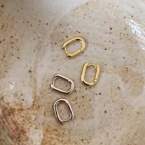 Detailed view of oval geometric hoop earrings in polished gold and silver finishes