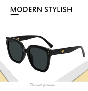 Detail of black oversized sunglasses with gold metal rivets and side logo on a white base