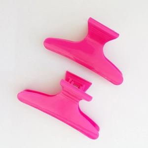 Dettaglio di due mollette per capelli rosa da 8cm in plastica per lo styling su bianco