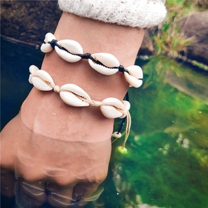 Detail of handmade woven shell bracelets in black and cream on wrist over stream