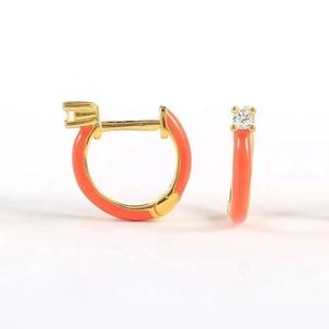 Macro detail of gold hoop earrings with coral orange enamel and clear zircon stones