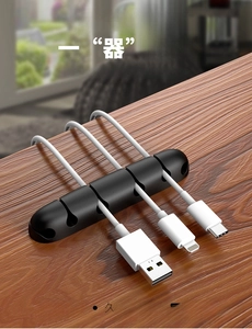 Macro detail of 5-slot black silicone cable organizer fixed on wood desk edge