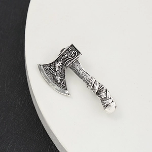 Silver vintage axe brooch with intricate carvings and textured handle on a white plate