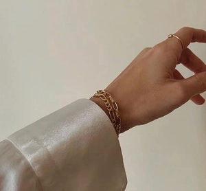 Detalle de pulseras de cadena Figaro y clip doradas superpuestas en una muñeca