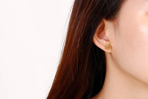 Gros plan d'un mannequin portant des boucles d'oreilles cœur doré ajouré au design épuré