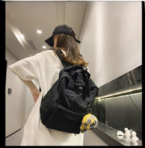 Detailed back view of a black canvas backpack featuring a cute yellow hat pendant