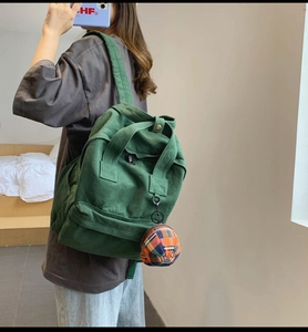 Rear view of model wearing a green canvas backpack with a plaid pom pom charm detail