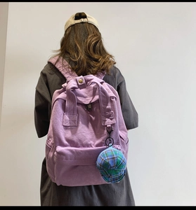 Rear view of a woman wearing a purple canvas backpack with a plaid hat charm