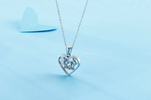 Detail view of silver hollow heart necklace with mae engraving on light blue background