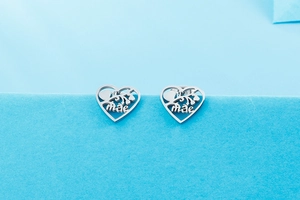 Macro shot of silver heart-shaped stud earrings with Mae engraving and floral patterns