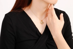 Detail shot of a hollow gold heart pendant necklace on a model wearing black V-neck top