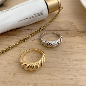Detailed view of two twisted croissant rings in gold and silver finish on wood surface