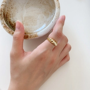 Detailed view of wide curved twisted croissant gold ring worn on hand with ceramic decor