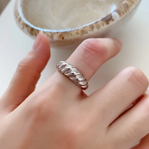 Macro detail of silver croissant twist ring featuring modern curved texture on model finger