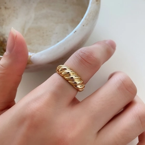 Close-up of golden croissant style ring on finger with warm home background