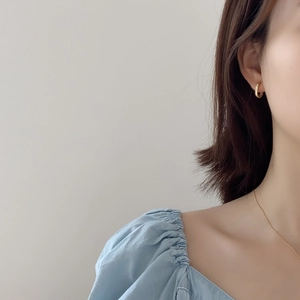 Close-up of minimalist gold oval hoop earrings worn by a model with a blue blouse