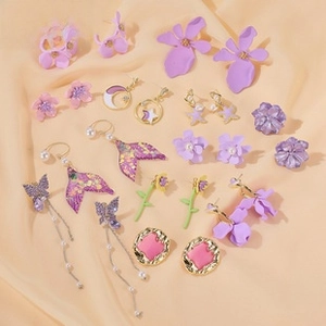 Flat lay of lavender floral earrings, butterfly tassels, and pearl studs on silk fabric
