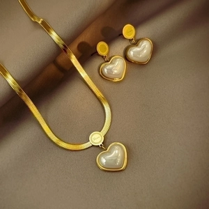 Detail of gold heart pendant and earrings set on silk with Love engraving