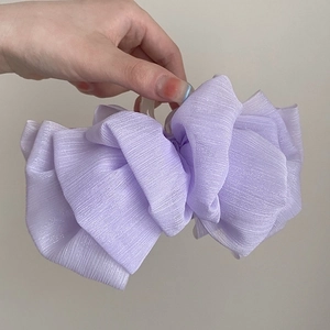Close-up of a lavender pleated fabric hair claw clip held by hand against a grey background
