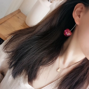 Close-up of sweet cherry earrings with resin dried flowers worn by a model in soft light
