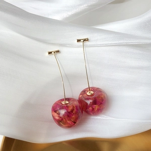 Detail of cherry-shaped long earrings with dried flower petals in resin and gold stems