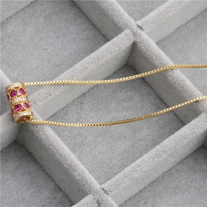 Détail d'un pendentif cylindre doré avec zircon rouge serti sur un fond en velours gris