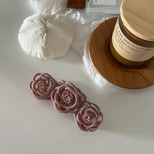 Detail of matte dusty rose hair claw clip with triple rose design on a wooden tray