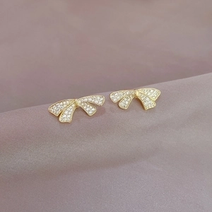 Elegant gold bow earrings with pavé crystals on purple velvet background flat lay view