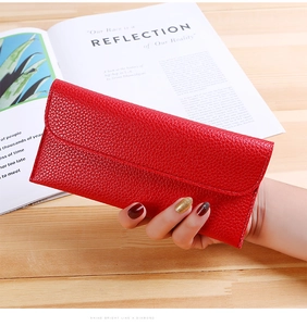 Red long flap wallet with litchi grain texture held by a hand on a wooden table