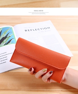 Close-up of stylish orange lychee pattern leather long wallet held by hand on a wooden desk