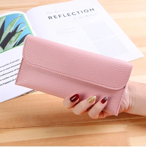 Close-up of a pink long wallet with lychee leather texture held against a magazine