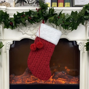 Chaussette de Noël en tricot rouge et blanc avec pompons accrochée à une cheminée
