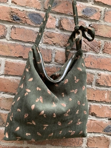 Detail of green corduroy crossbody bag with leaf print hanging on a red brick wall