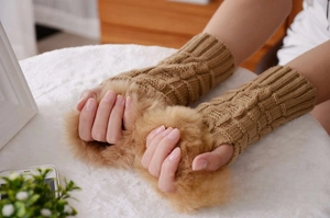 Detail of camel knitted fingerless gloves with fluffy faux fur cuffs and cable knit pattern
