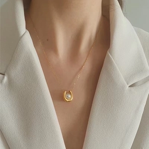 Detail shot of a golden U-shaped pendant with a white pearl on a delicate fine chain