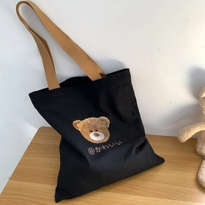 Black canvas tote bag with cute brown bear print and shoulder straps on a wooden surface