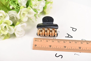 Close-up of a 4cm black glitter acrylic hair claw clip with golden metal grip detail