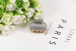 Detail of a small grey glitter acrylic hair claw clip with golden metal spring
