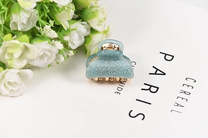 Detailed view of a light blue glitter resin hair claw clip with gold metal spring