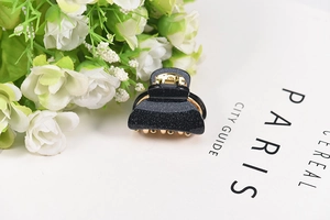 Close-up of a small black acrylic hair claw with fine glitter and golden metal spring
