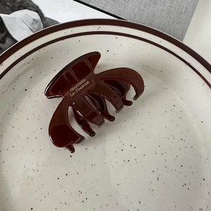 Close-up of a dark brown amber hair claw clip with gold lettering in a ceramic bowl