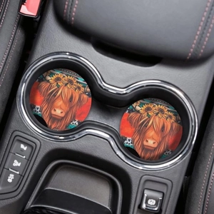 Close-up of two highland cow coasters with sunflower accents in a car cup holder