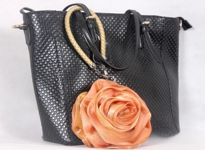 Detail of black woven texture handbag featuring a large orange silk rose ornament