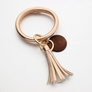 Detail van roségouden kunstlederen armband met kwastje en ronde donkere houten hanger