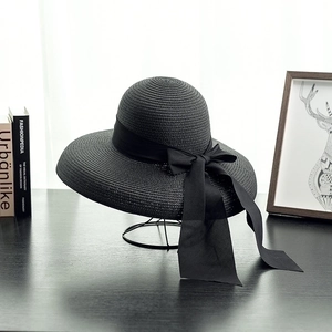 Elegant black straw sun hat with long bow ribbon on metal stand for summer beach trips